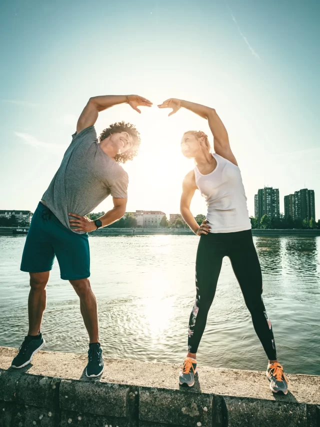 young-happy-couple-is-training-outdoors-by-river-stretching-together-wall-sunset